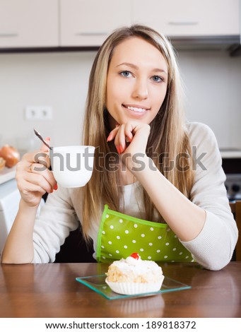 Pretty woman drinking tea with cake at table in home kitchen