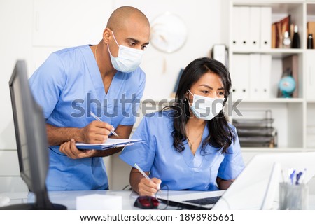 Doctor and nurse in protective medical mask check patient data in hospital computer database