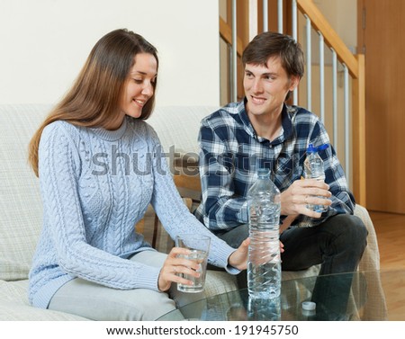 Happy couple drinking bottled water in home