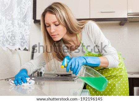 Blonde housewife cleaning furniture in kitchen with detergent