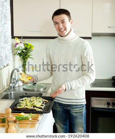 Smiling man putting pieces lemon in fish at home kitchen
