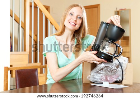 Smiling young woman with new electric coffee maker at home