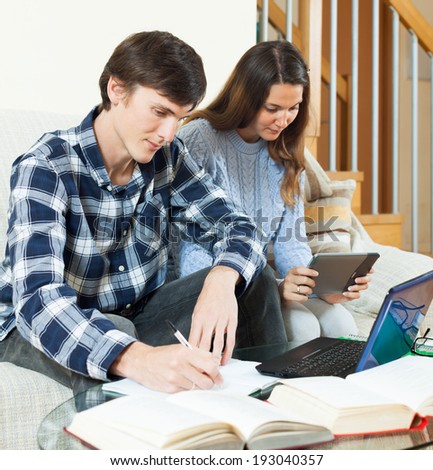 Couple serious students learning for exam with electronic book in home interior
