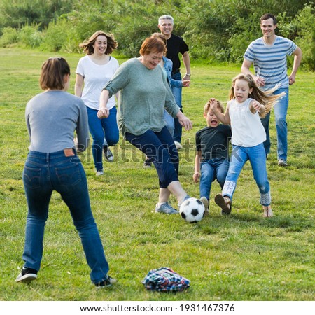 Cheerful males and females kicking the ball on green lawn