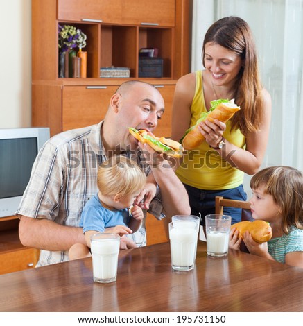 Happy family of four having lunch with sandwiches at the table