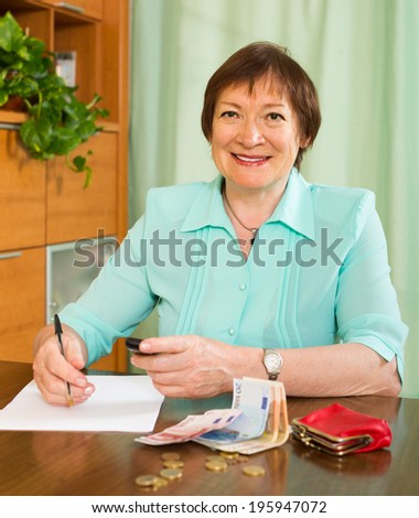 Happy senior woman sitting at the table with money and documents