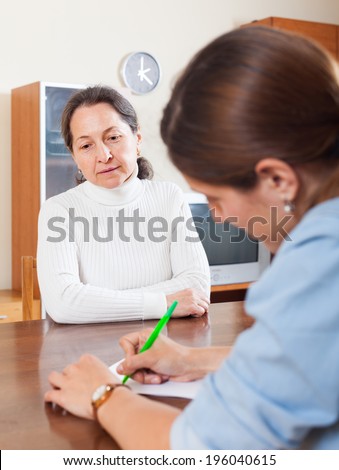 Sad mature woman answer questions of social worker in home