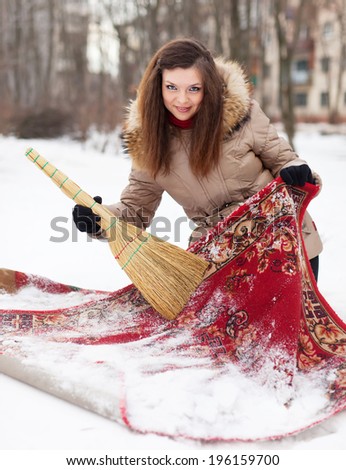 woman cleans red carpet with snow in winter day