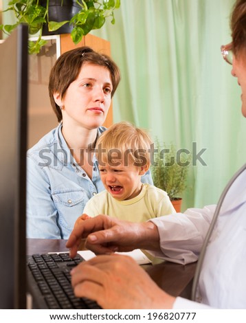 Mature female pediatrician doctor examining crying toddler at clinic
