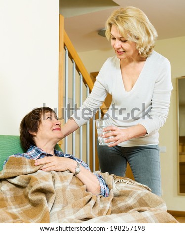 elderly woman offering medicine and water to pensioner at home