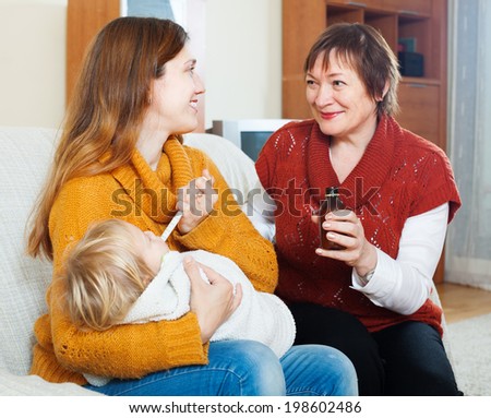 Young woman with mature mother giving cough syrup to unwell baby at home