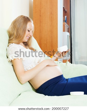 Blonde pregnancy woman caring for skin with cosmetic cream in home