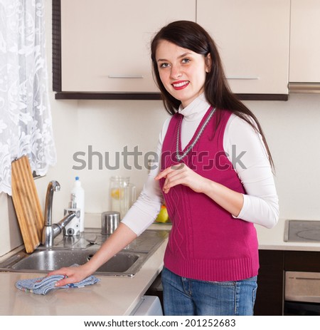 Smiling housewife cleaning  furniture with rag in kitchen at home