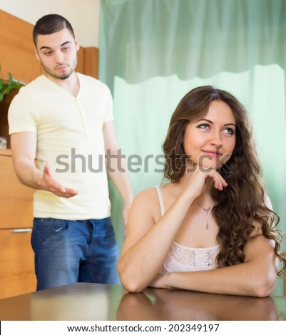 Casual young couple having serious talking at table in living room. Focus on cunning woman