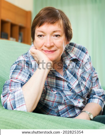Stressed female pensioner laying on her elbows and thinking  on couch