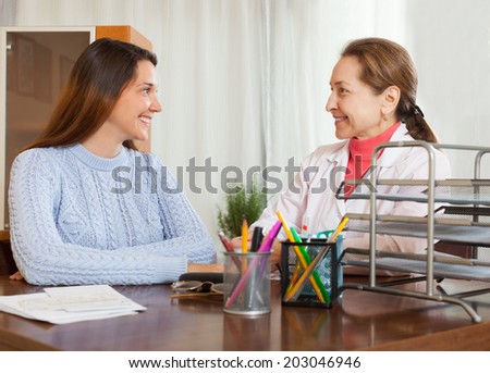 Friendly female doctor and teenager patient talking at table