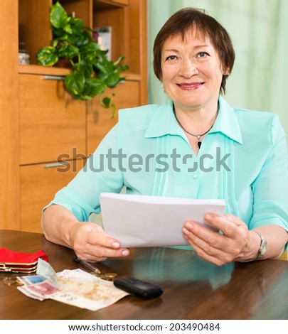 Positive elderly woman with financial documents and money indoors