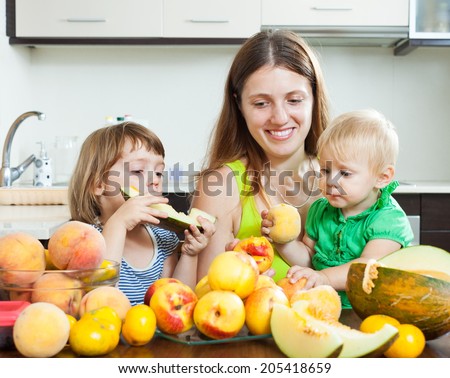 Happy woman with daughters together with melon and peaches over dining table at home