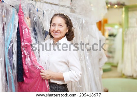 Happy mature woman  chooses dinner gown at boutique