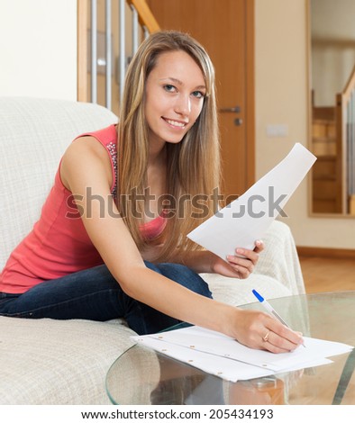 Happy young woman sitting on couch with homework and pen at home