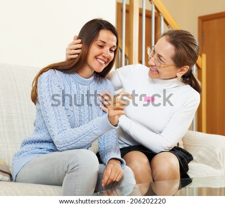 Happy mother and adult daughter with pregnancy test at home interior