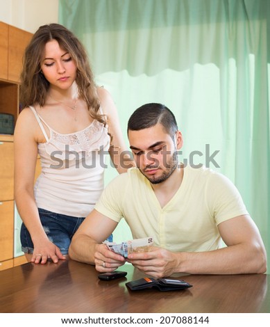 Financial problems in young family. Man counting money, woman watching him in home