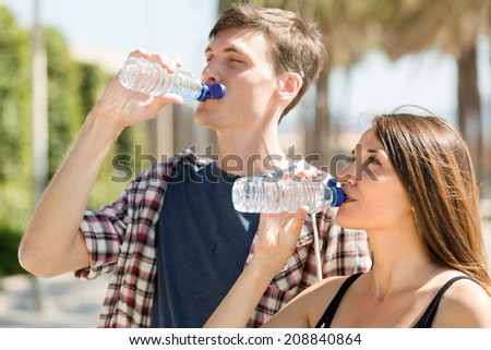 Thirsty young male with girlfriend drinking water from bottle at sunny day