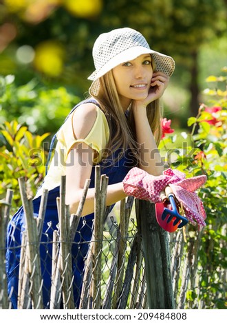 gardener in blue uniform  in summer garden near fence