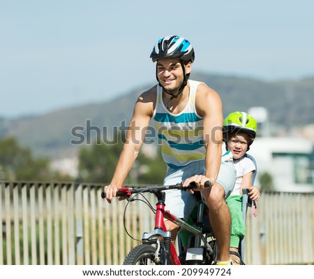 Happy young father with daughter in helmets cycling though street