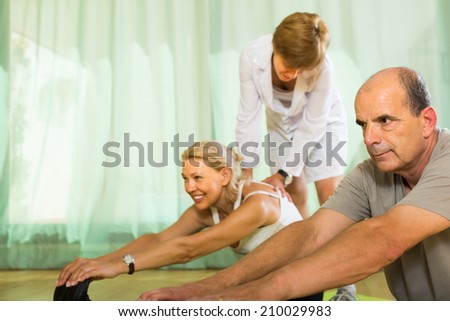Medical staff at gym helping mature couple to take correct position. Focus on man