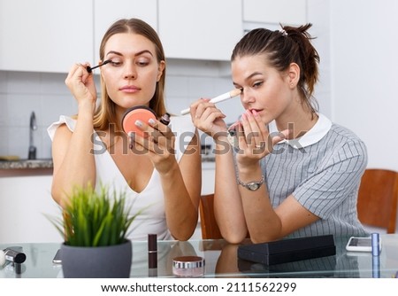 Two positive young female friend doing make up at table with cosmetics in kitchen Сток-фото © 