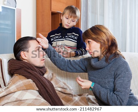 Woman and son caring for ilness man who has high temperature at home