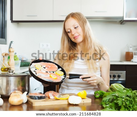 Smiling woman cooking salmon fish with lemon on griddle at  kitchen
