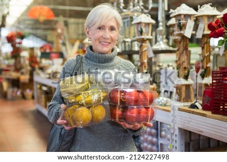 Smiling senior woman having fun choosing colorful festive Christmas decorations for home interior on holidays eve in store ストックフォト © 
