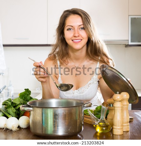 Ordinary young woman cooking soup in home kitchen