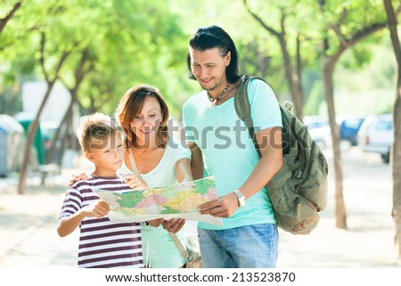 Happy family of three searching way at paper map in the city park