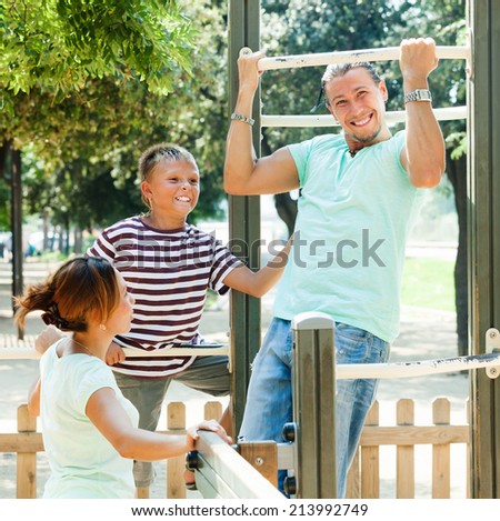 Middle-aged man with family training on chin-up bar in the yard