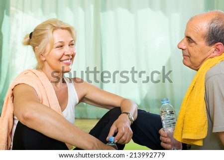 Active elderly spouses with bottles of water after morning exercises. Focus on woman