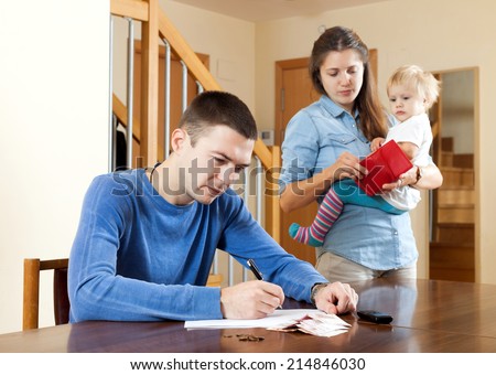 Financial problems in family. Sad woman wit baby against husband at table with money