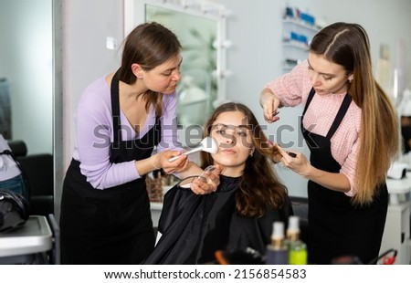 Portrait of interested young woman visiting professional beauty parlor. Skilled female hairdresser doing hairstyling, makeup artist applying makeup to client Stok fotoğraf © 