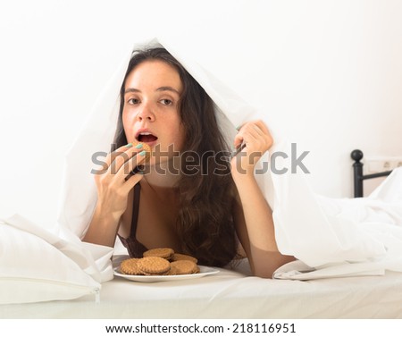 Brunette girl eating chocolate chip cookies in her bed at home