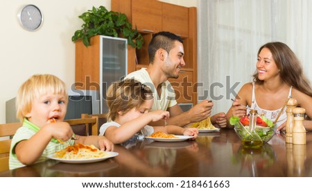 Young smiling family of four having lunch with spaghetti at home. Focus on girl