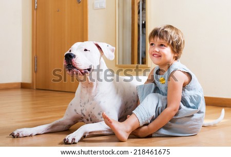 Positive smiling little girl with big white dog on the floor at home