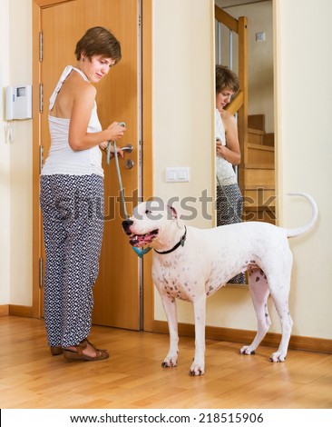 Smiling female owner with dogo Argentino on leash staying at door