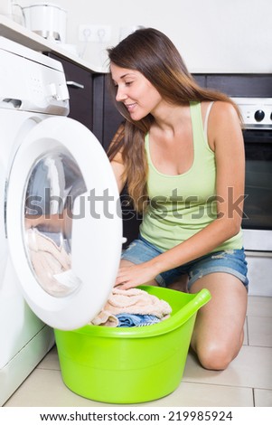 Home laundry. Happy young girl  loading clothes into washing machine  in home