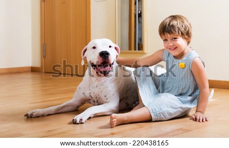 Happy smiling little girl with big white dog on the floor at home