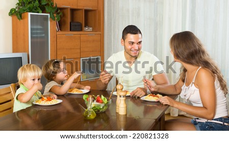 Happy young family of four eating with spaghetti at table. Focus on man