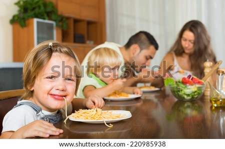 Young family with playful kids eating with spaghetti at table. Focus on girl