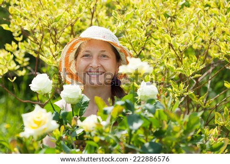 Happy mature woman in yard gardening with roses plant