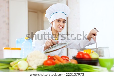 Portrait of  happy female cook in white works with ladle at commercial kitchen